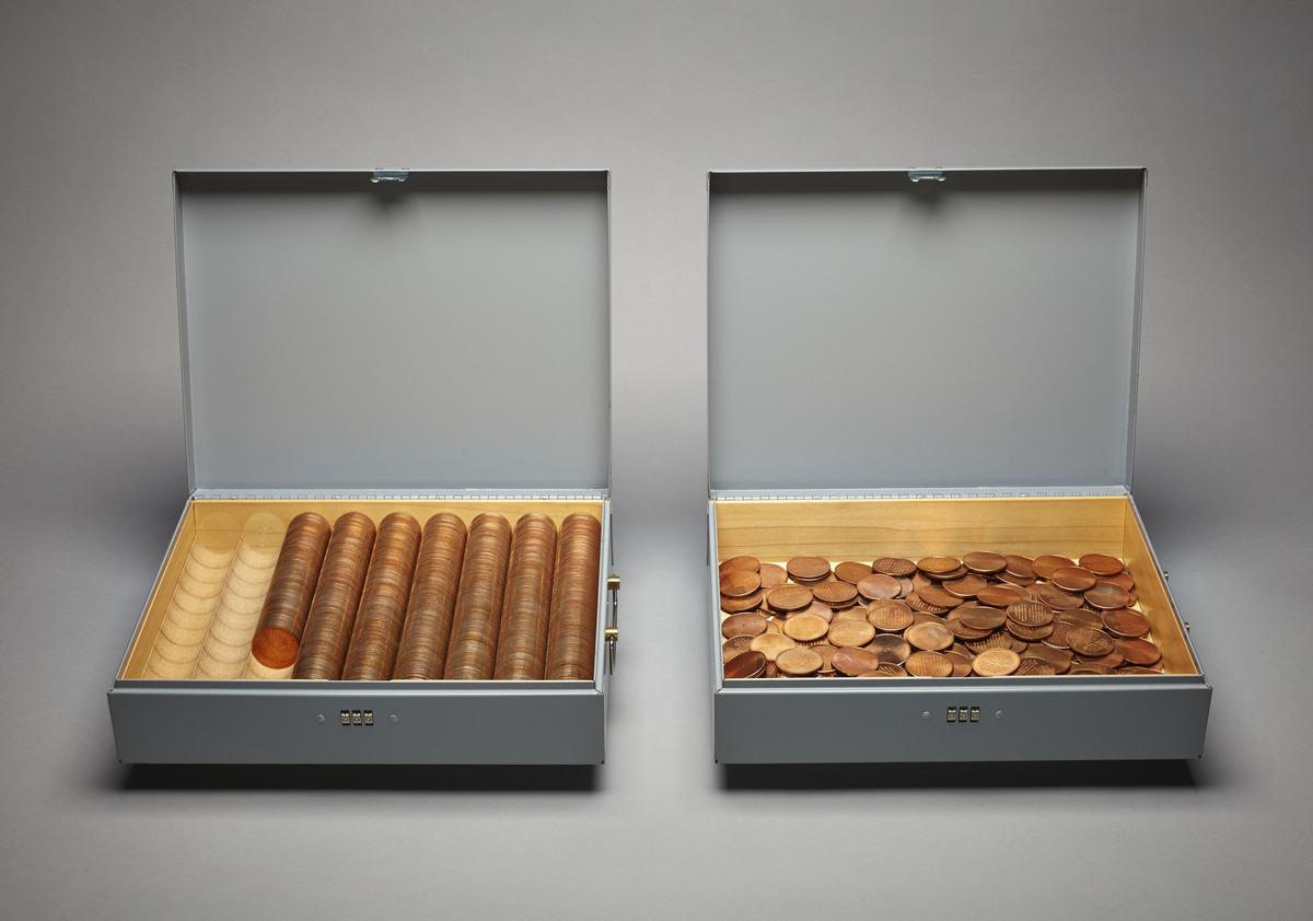 An image of Micah Lexier's work in the form of a quantity of coins equal to the number of months of the statistical life expectancy of a child born January 6, 1995. It features two gray metal boxes with organized coins in the left box and scattered coins on the right