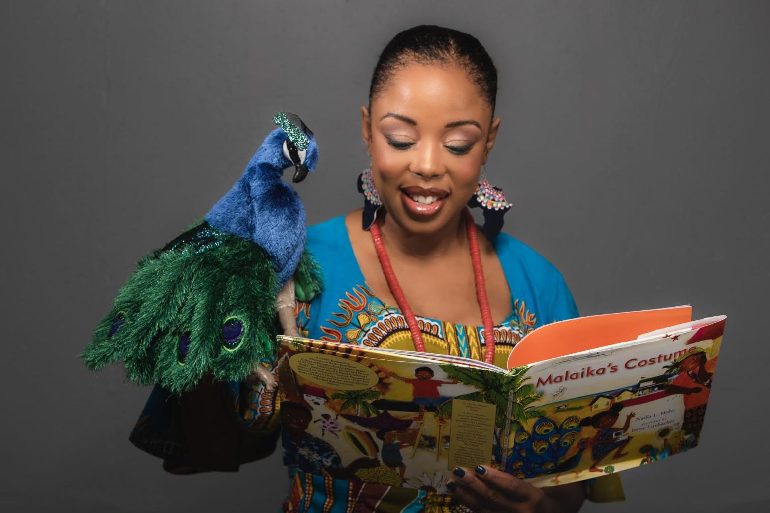 An photo of Nadia Hohn reading her book Malaika's Costume with a peacock puppet