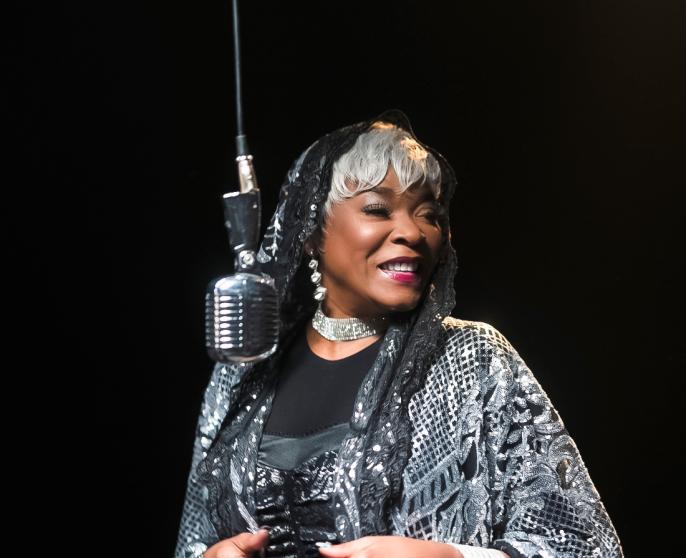 A photograph of Sharon Marley at an old school microphone dressed in a silver outfit