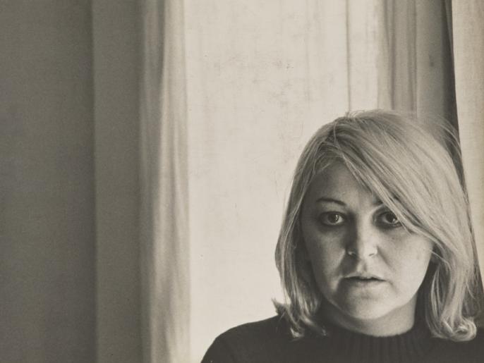 A black and white photo of Joyce Wieland in front of a curtained window