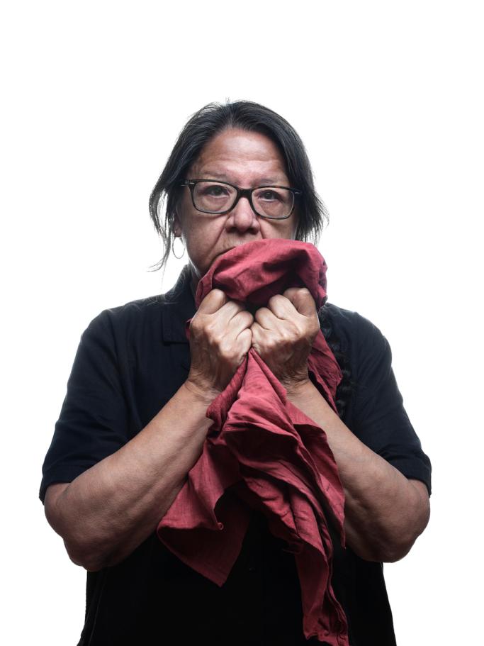 A portrait of artist Faye HeavyShield. She holds red fabric over the lower half of her face.