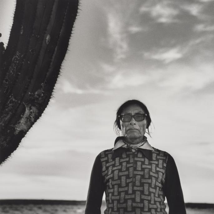 An image of Graciela Iturbide's photo  Desierto de Sonora, México. It features  a woman standing in a desert beside a cactus