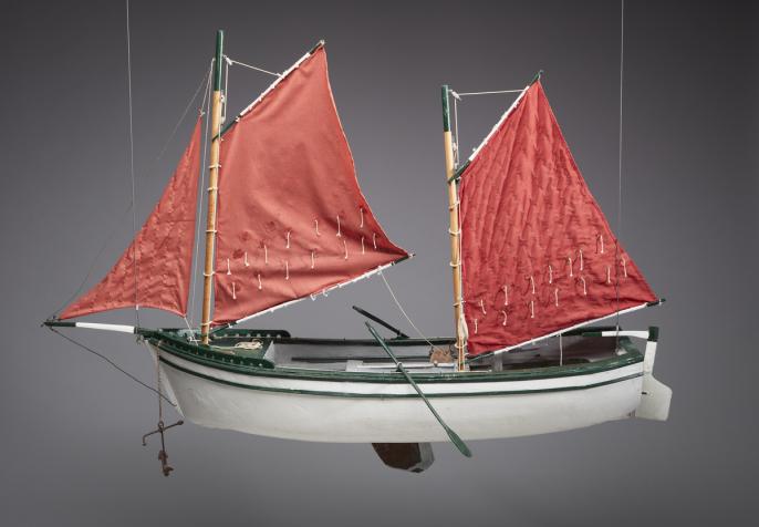 An image of Angus Trudeau's boat model red sailboat. It has a white hull with green trimmings and red sails.