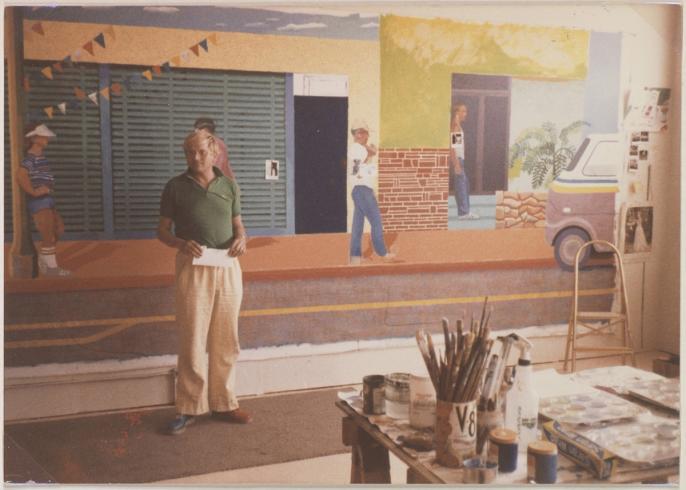 A man stands in front of a large horizontal painting on the wall behind him