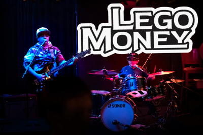 Two young boys playing instruments. One is playing guitar, the other is playing drums.