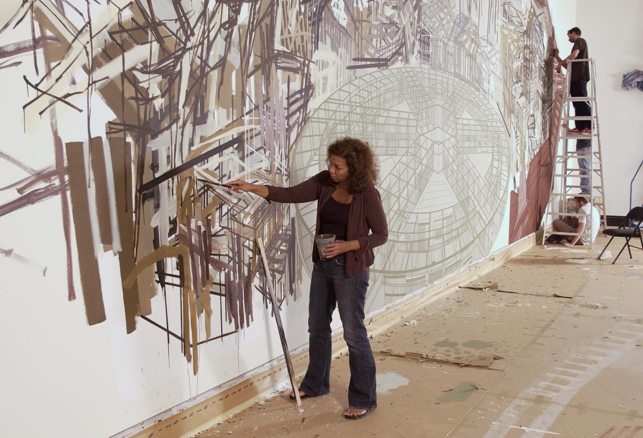 Denyse Thomasos painting a mural on a wall in the AGO