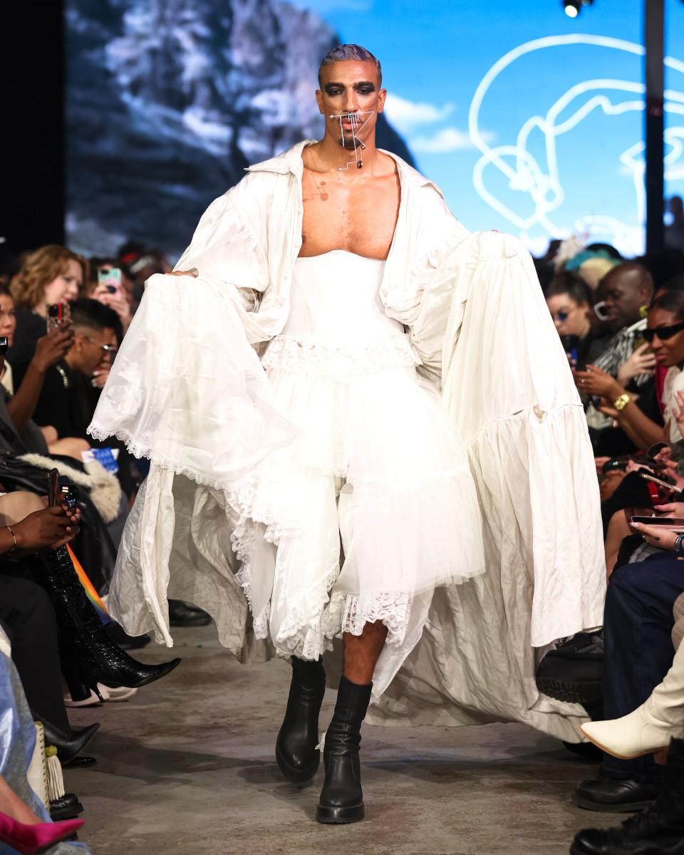 An image of a model walking down a runway in a white outfit designed by Mic Carter for their fashion line L’Uomo Strano