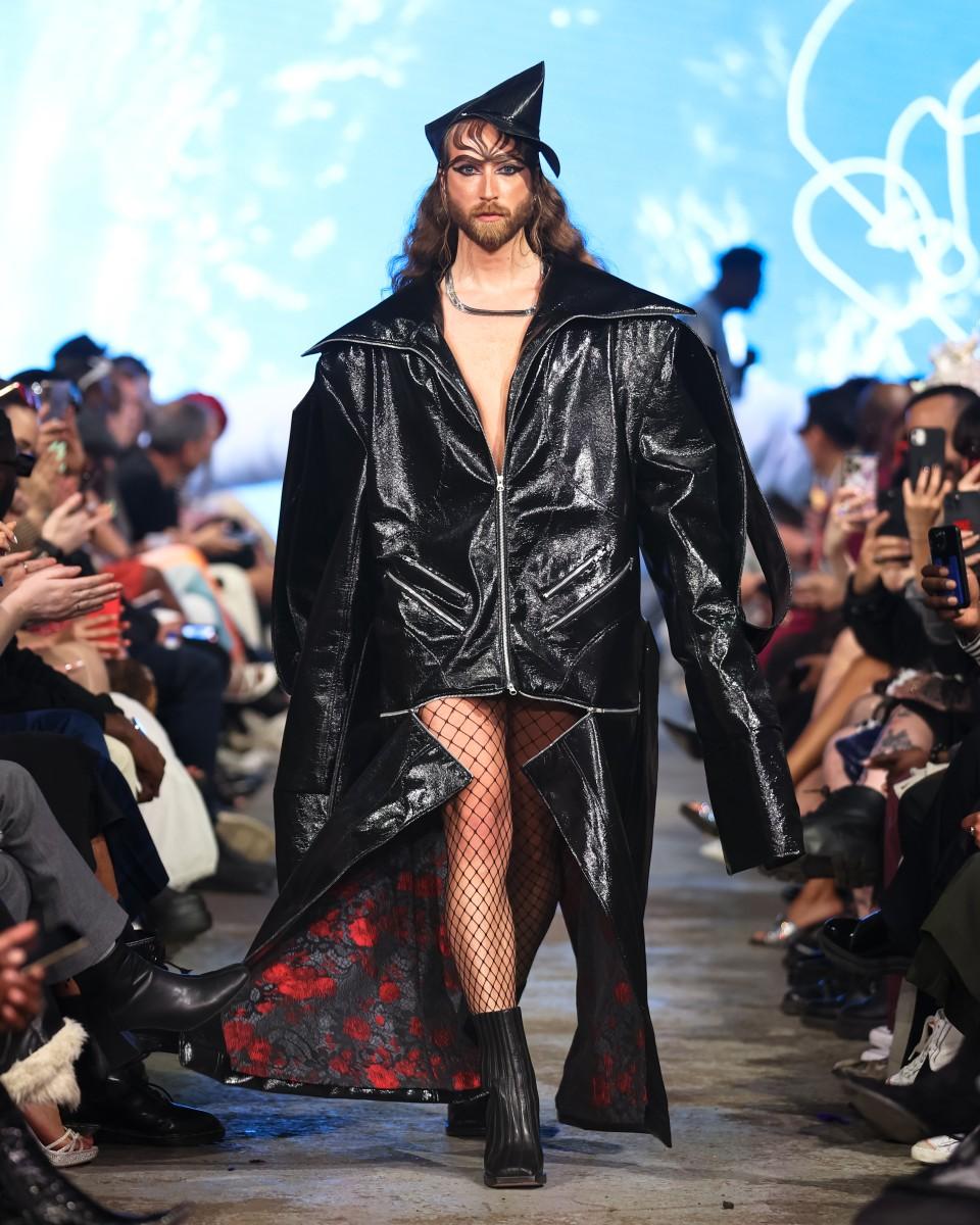 An image of a model walking down a runway in a Black leather outfit designed by Mic. Carter for their fashion line L’Uomo Strano