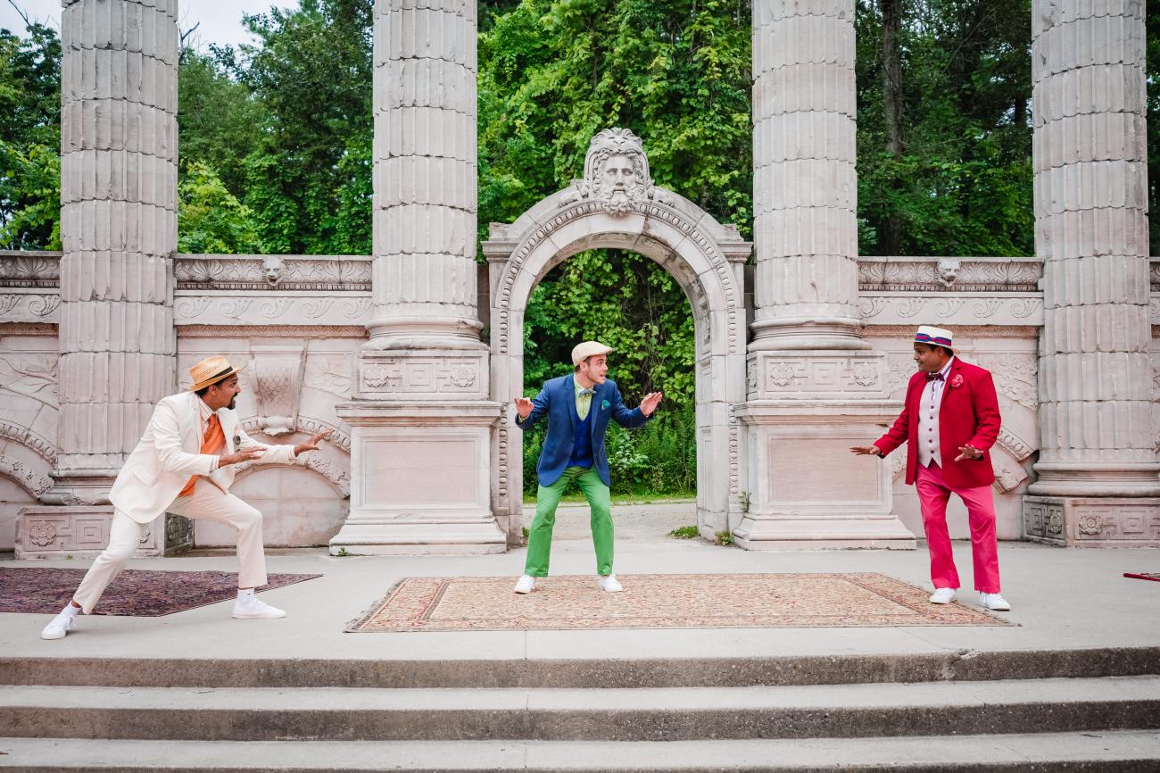 An image of Guild Festival Theatre's production of Three Men in a Boat, featuring three actors on a stage, one in a beige and orange suit, one in a blue suit, and one in a red suit.