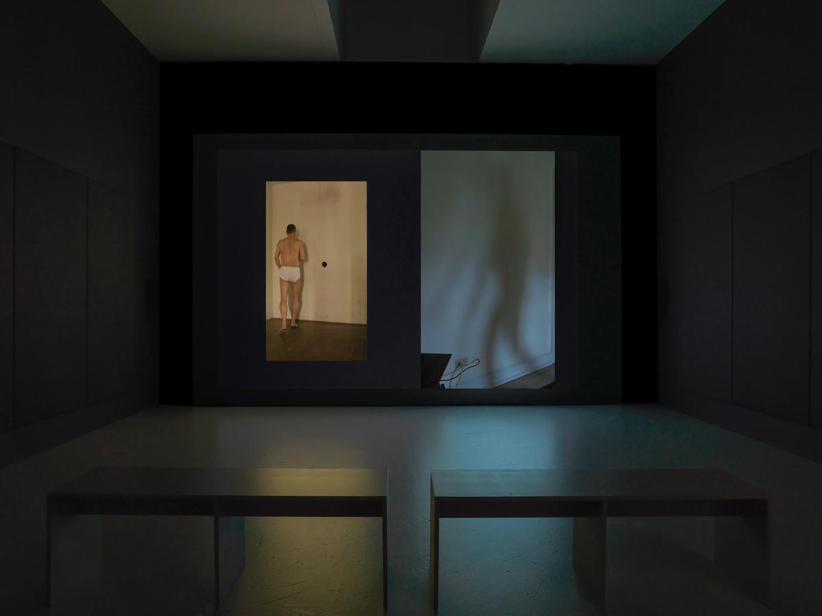 A still from Wolfgang Tillmans's video instrument, which features two adjacent videos, one with Tillmans in white briefs dancing with his back towards the audience and the second featuring Tillmans shadow similarly dancing