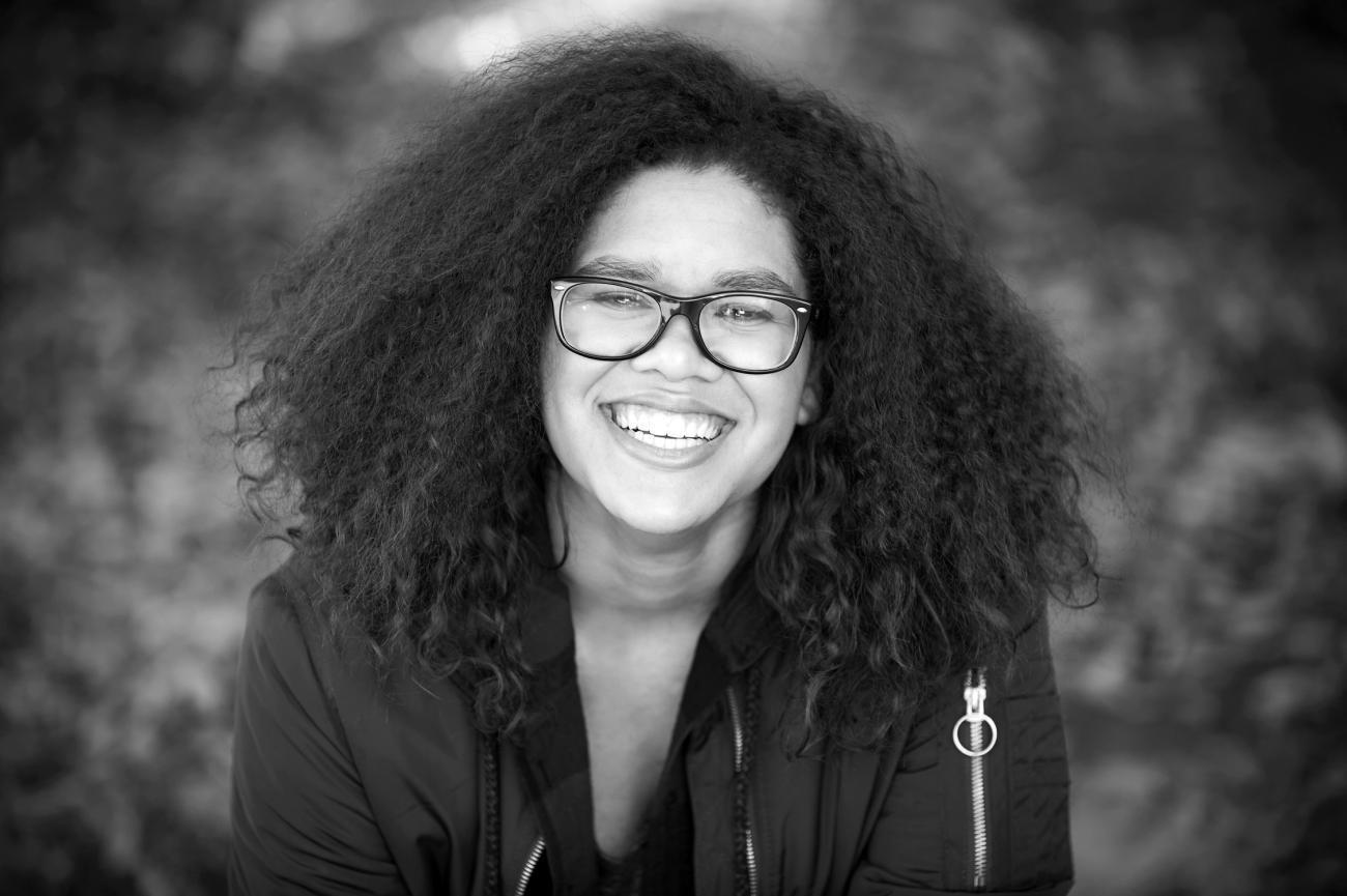 An image of photographer Rae RezWell in Black and white. She is smiling at the camera with her curly hair down