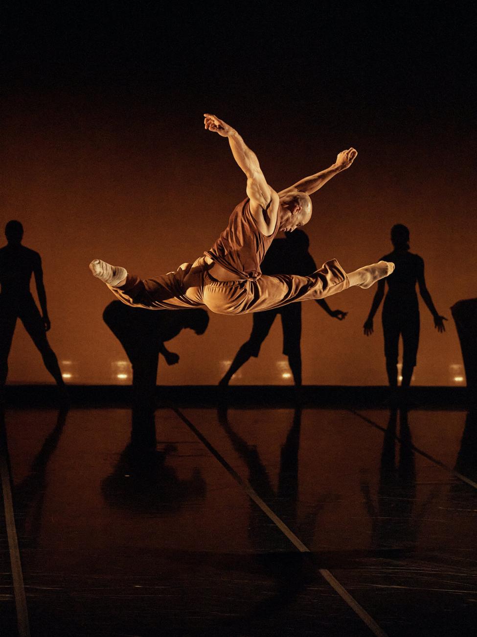 An image of a dancer mid air on stage with a background of dancers in various poses