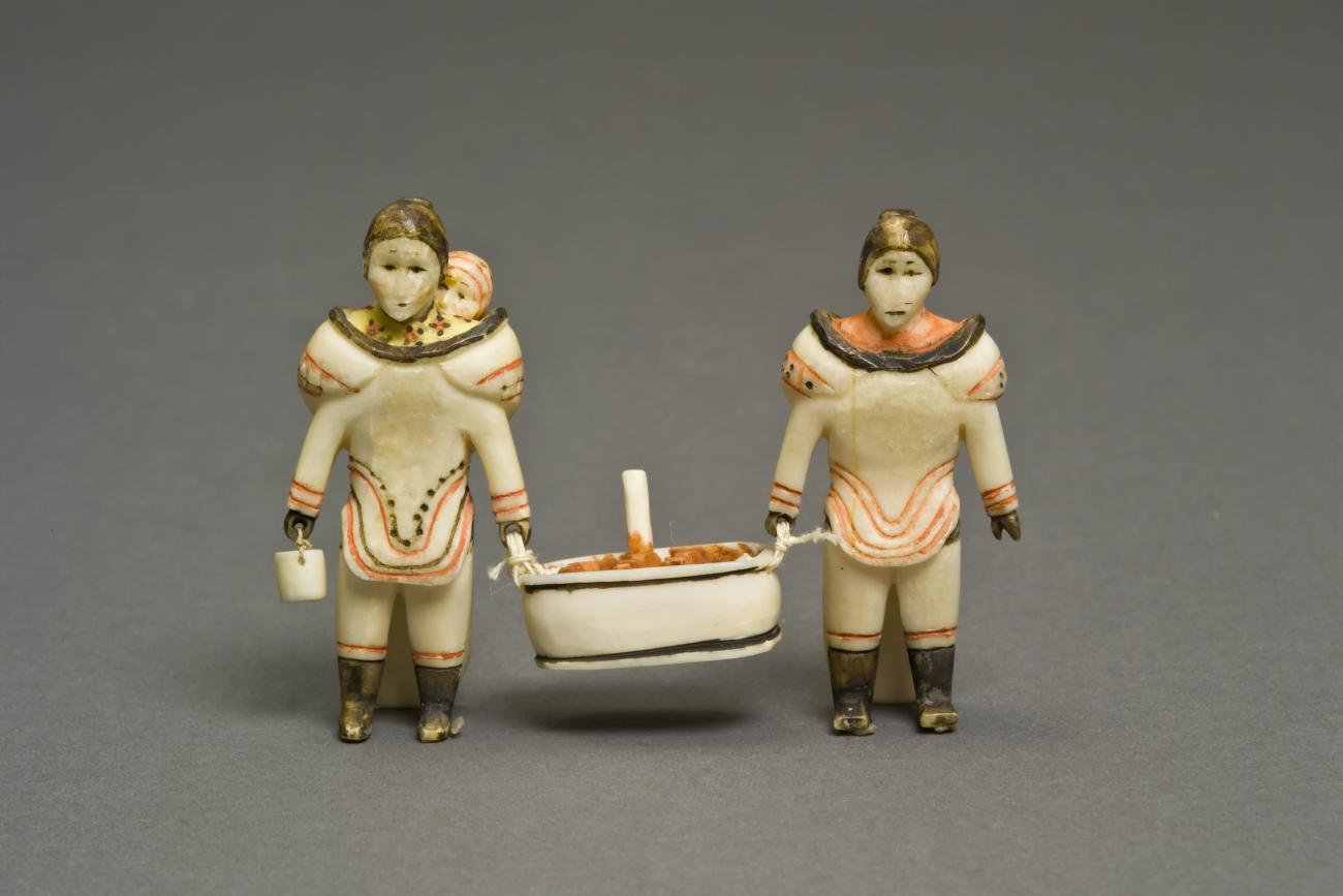 A sculpture of two women carrying meat in a tub. One woman has a baby on her bacl