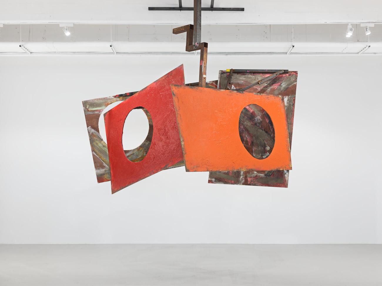 An installation of a series of metal red and orange panels with a circle cut-out hanging from the ceiling