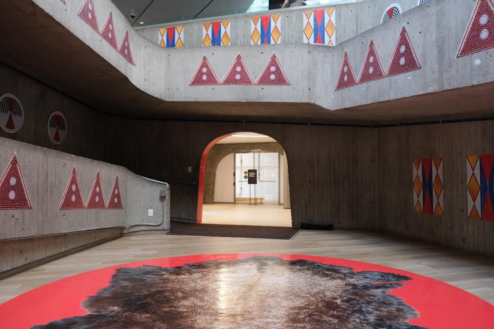 An installation image of Niitoyis, featuring a large vinyl of a buffalo hide on the floor, and images of bead work and parfleche on the walls
