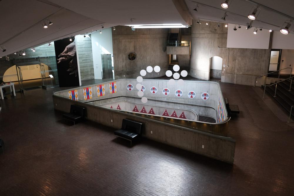 An installation shot of NINA, featuring racoon furs hanging form the ceiling and two beaded mannequins