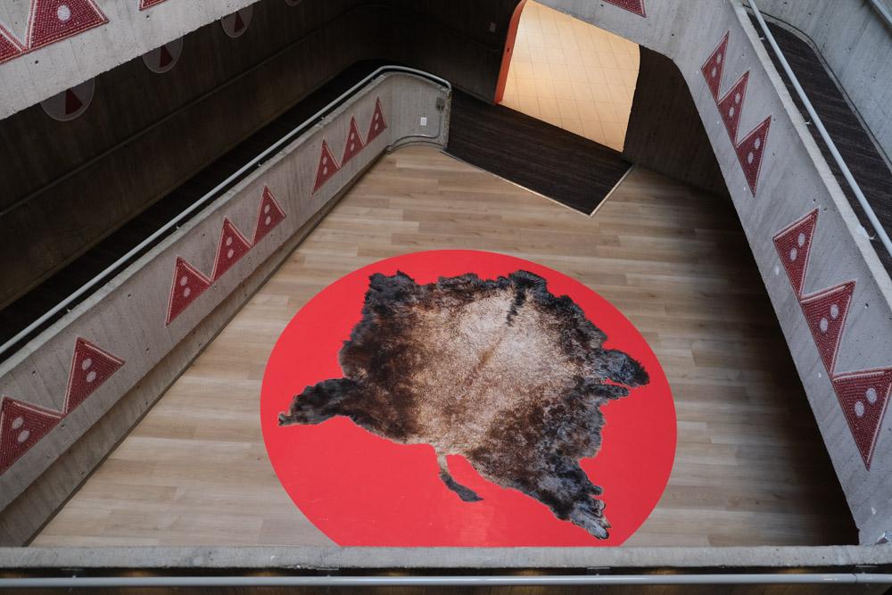 An installation image of Niitoyis, featuring a large vinyl of a buffalo hide on the floor, and images of bead work and parfleche on the walls