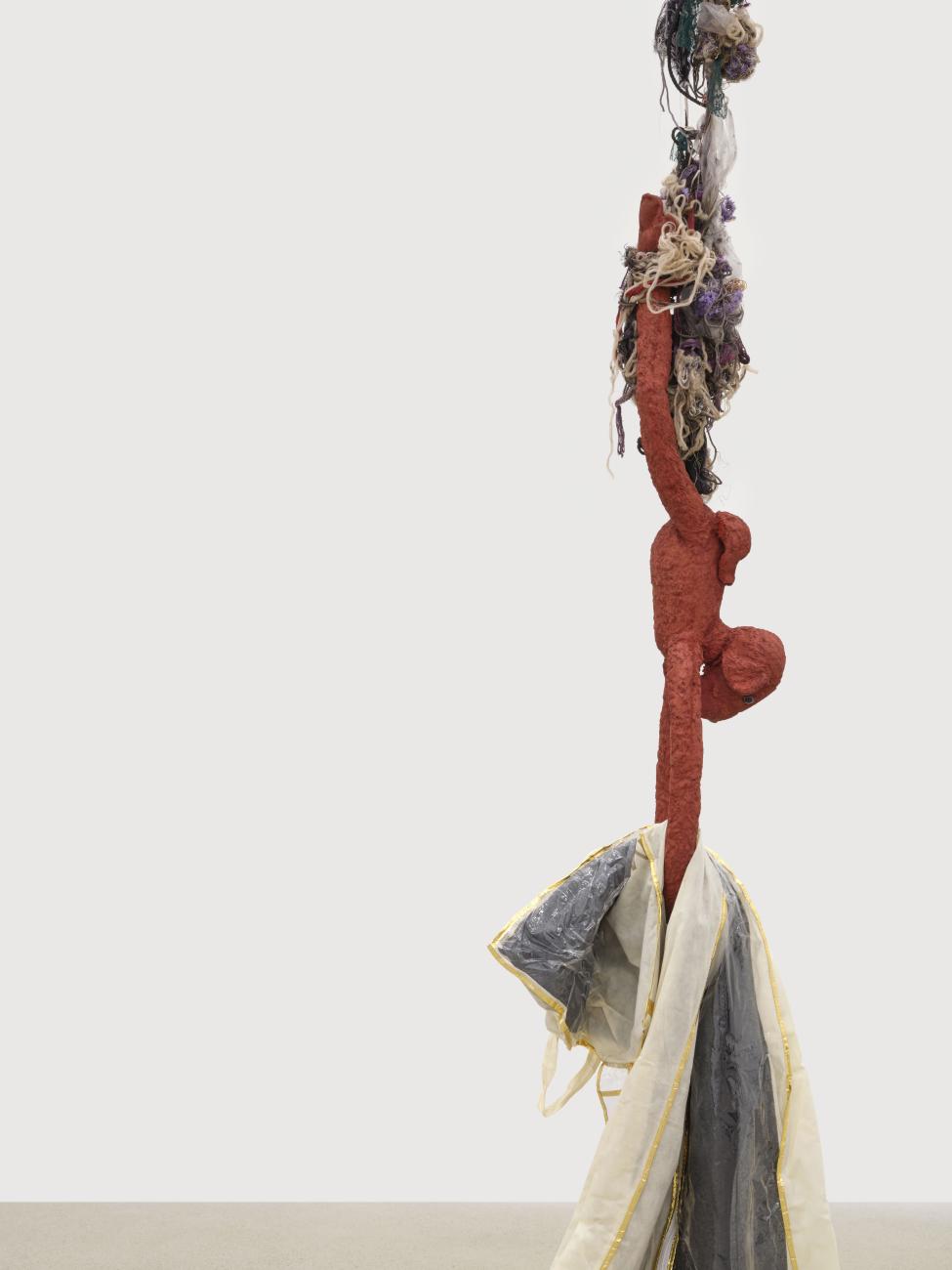 A monkey hanging upside down from a bundle of strings, holding a piece of fabric