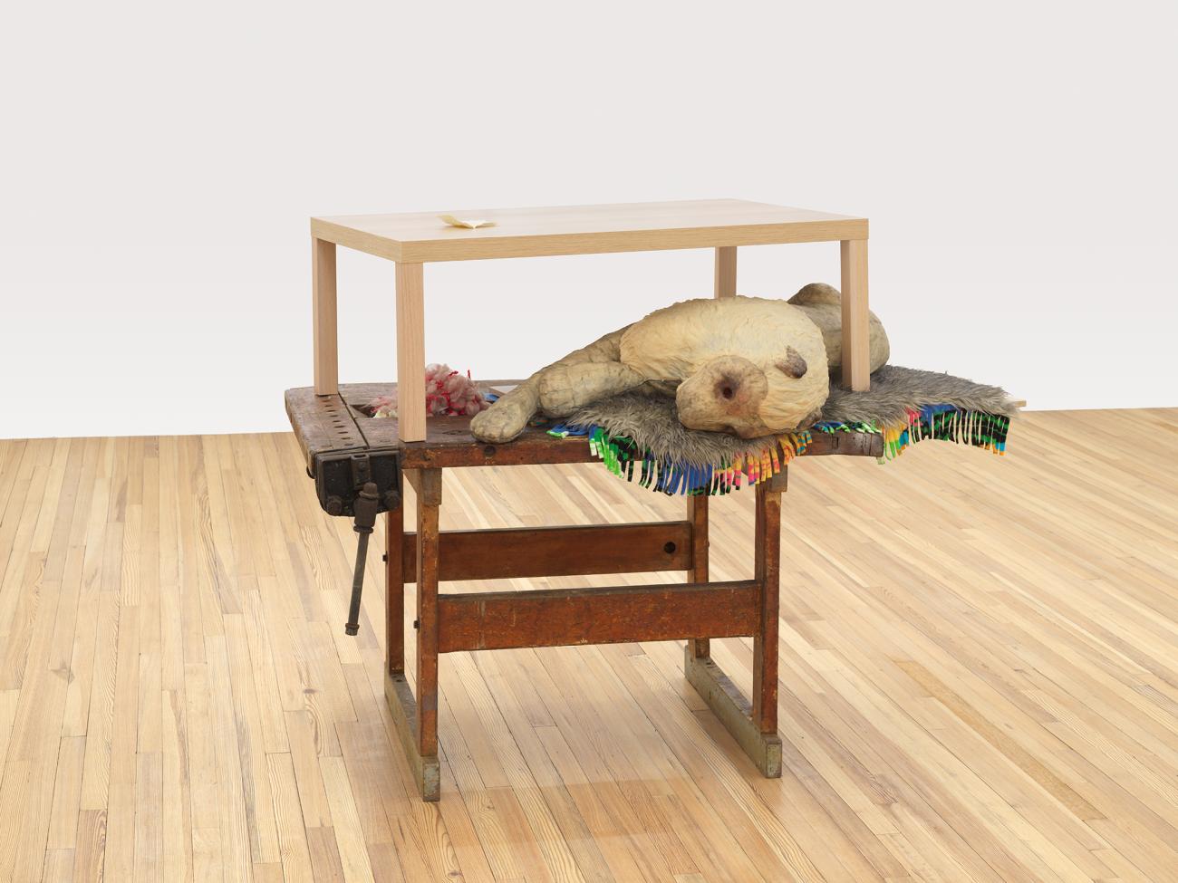 A sculpture of different tables stacked, with a lion laying between the two tables