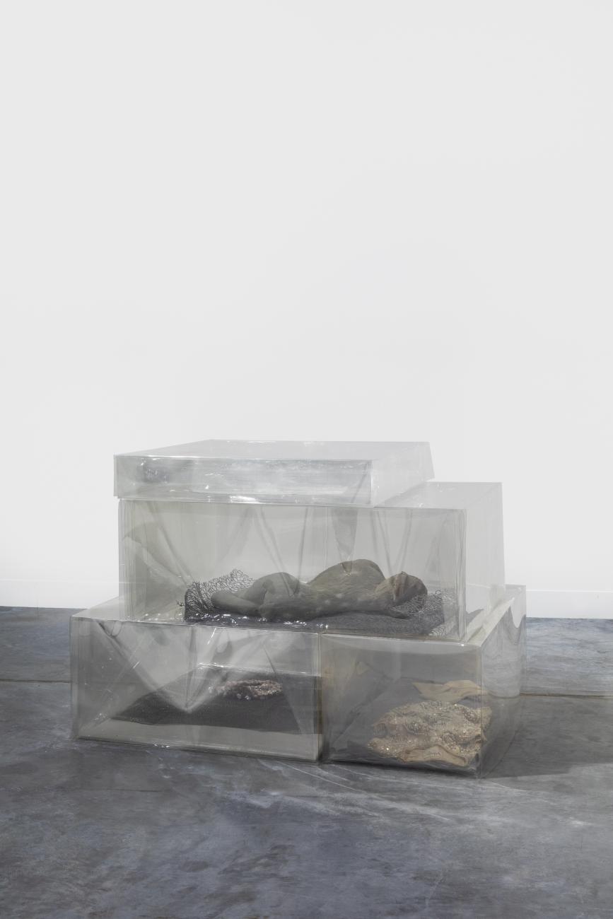 A sculpture made of a series of clear plastic boxes with various items inside