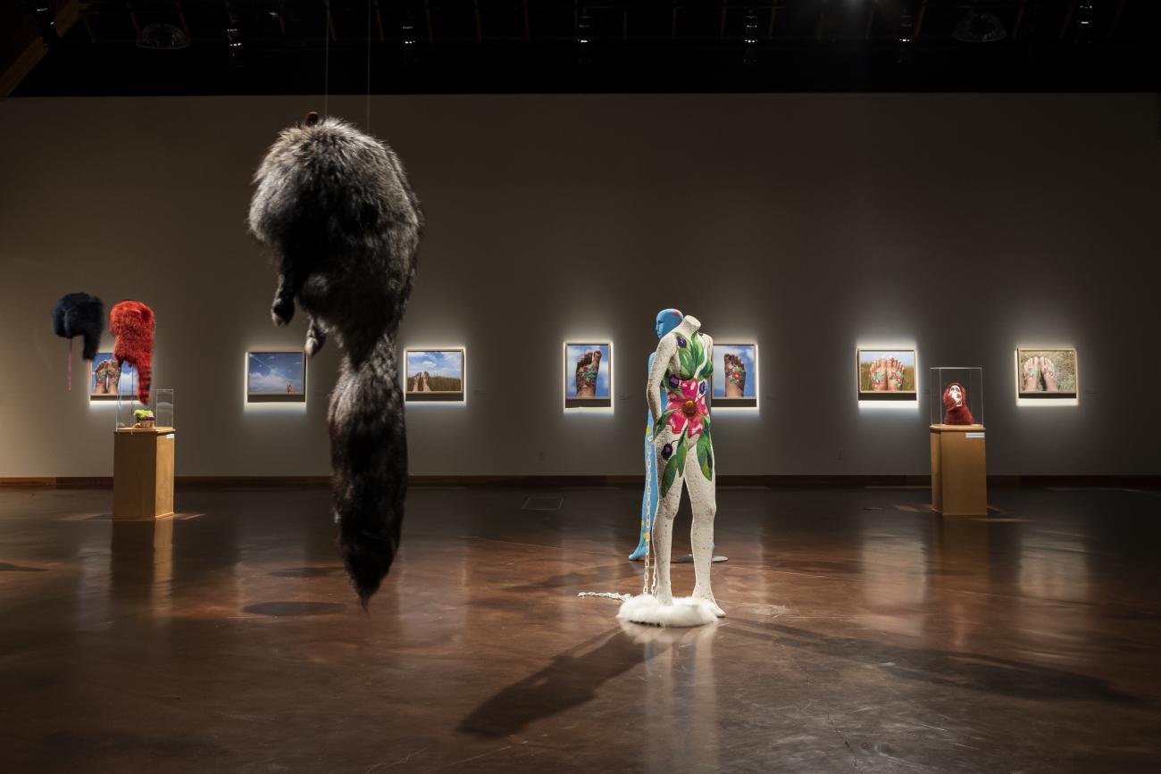 An installation shot of NINA, featuring racoon furs hanging form the ceiling and two beaded mannequins