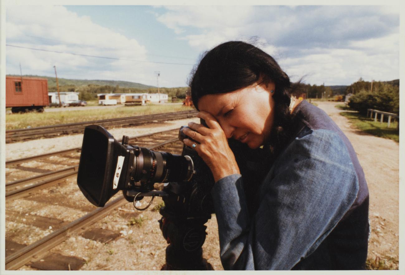 an image of filmmaker Alanis Obomsawin outside by railway track, filming with a camera