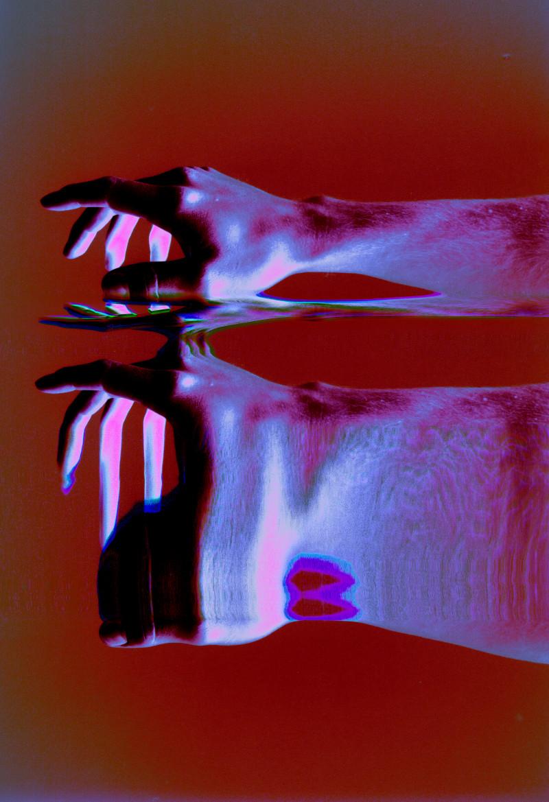 An image of a purple hand, the reflection of the hand ripples below it