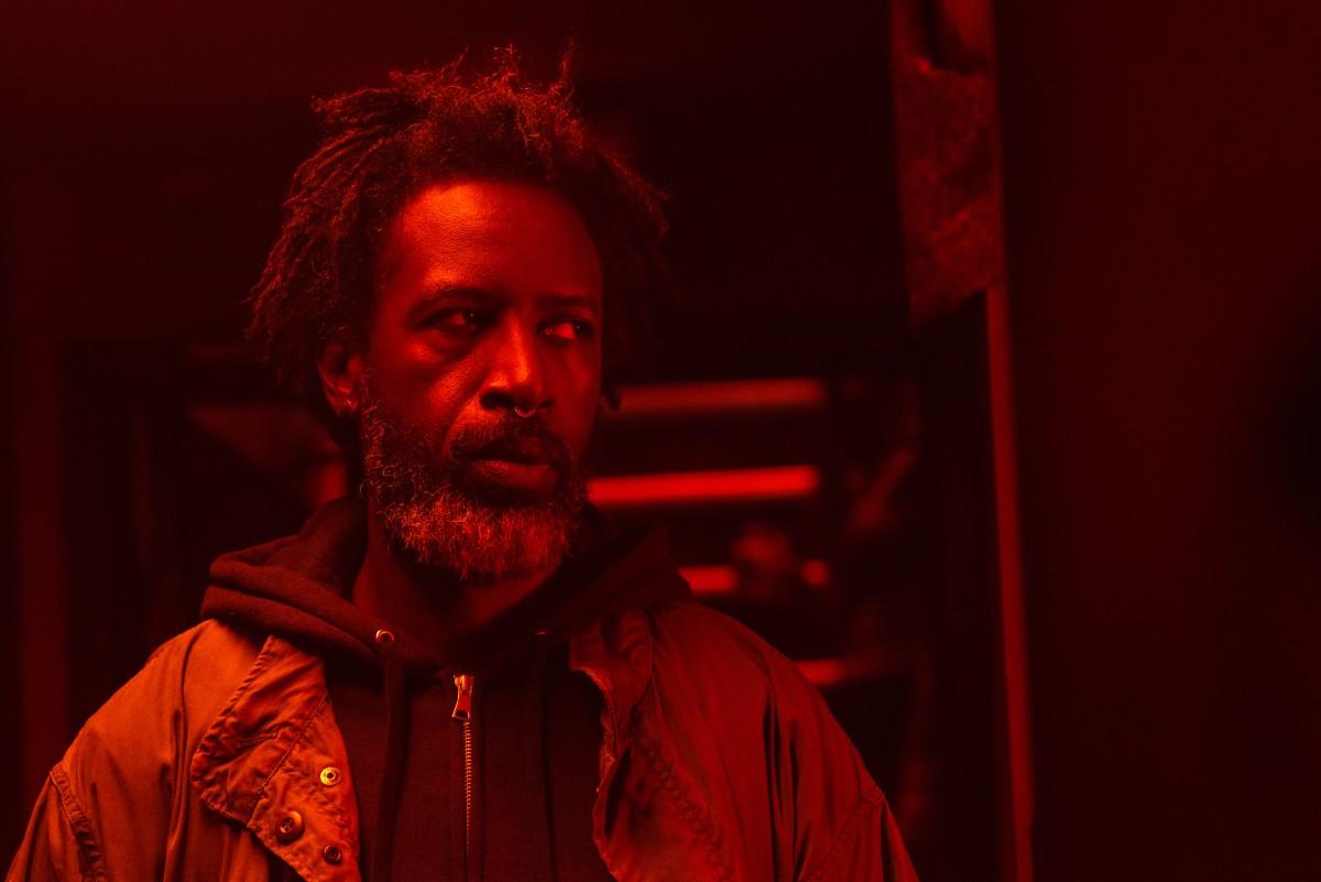Saul Williams looks off to the side. He wears a black hooded sweater and a jacket overtop.