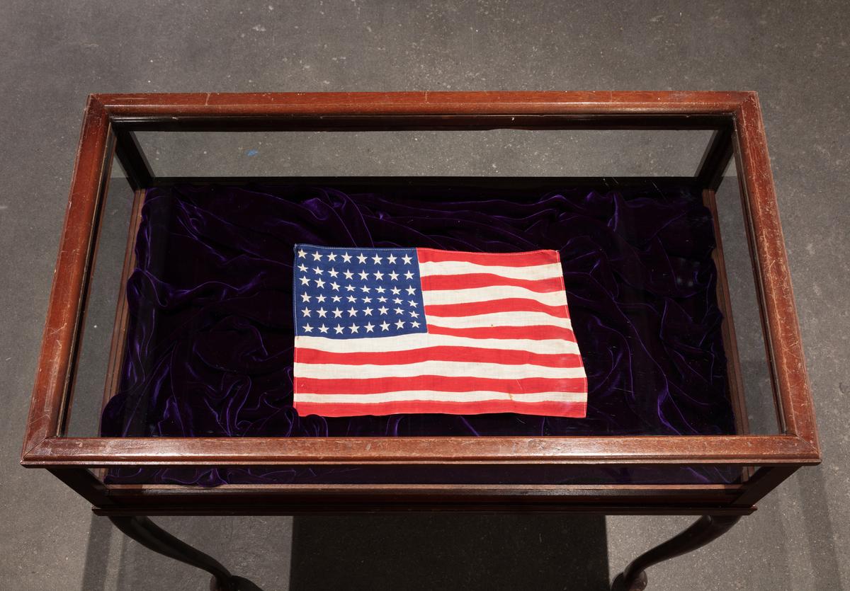 An American flag laid in a glass case with wood frame