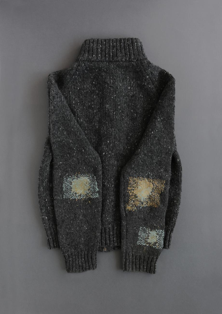 A photograph of a grey sweater with green and yellow mending at the elbows