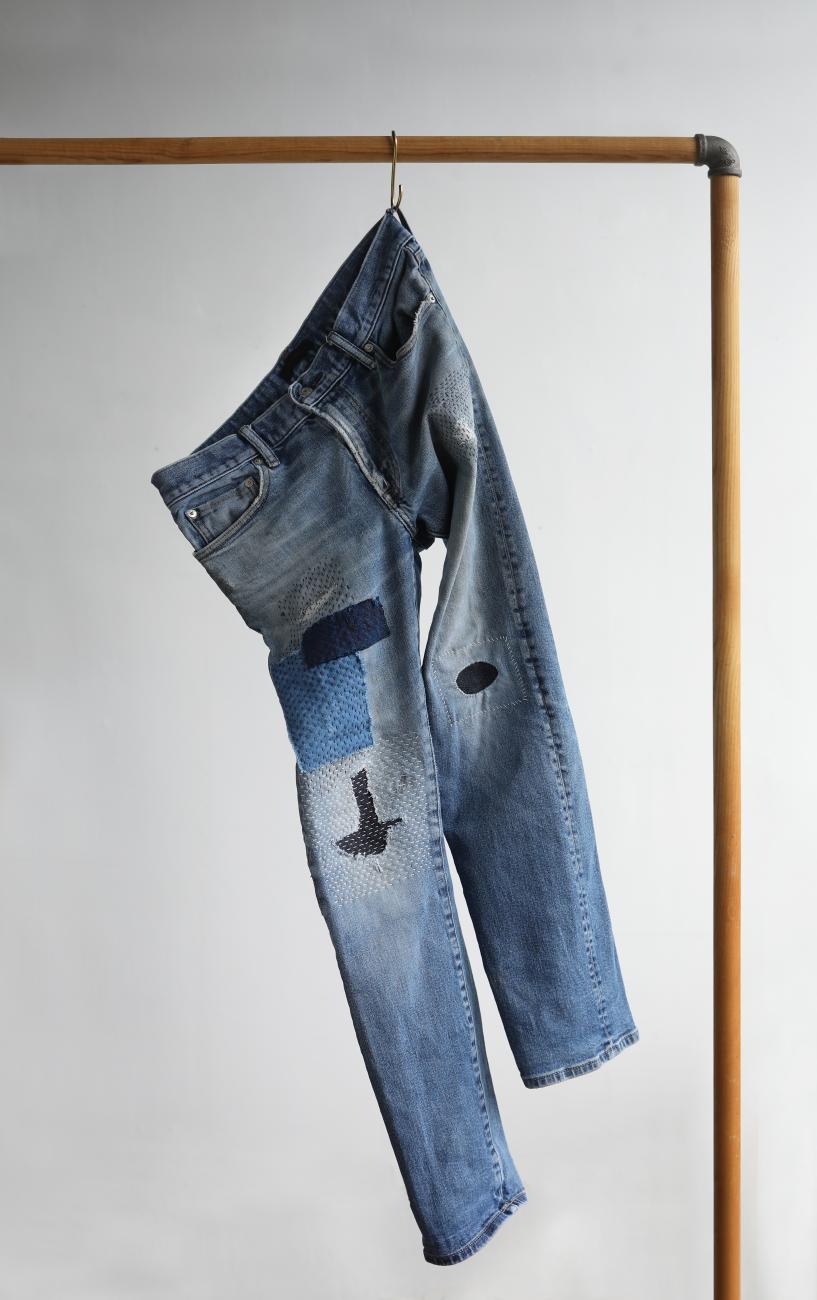 A photograph of a mended pair of jeans hanging from a rack