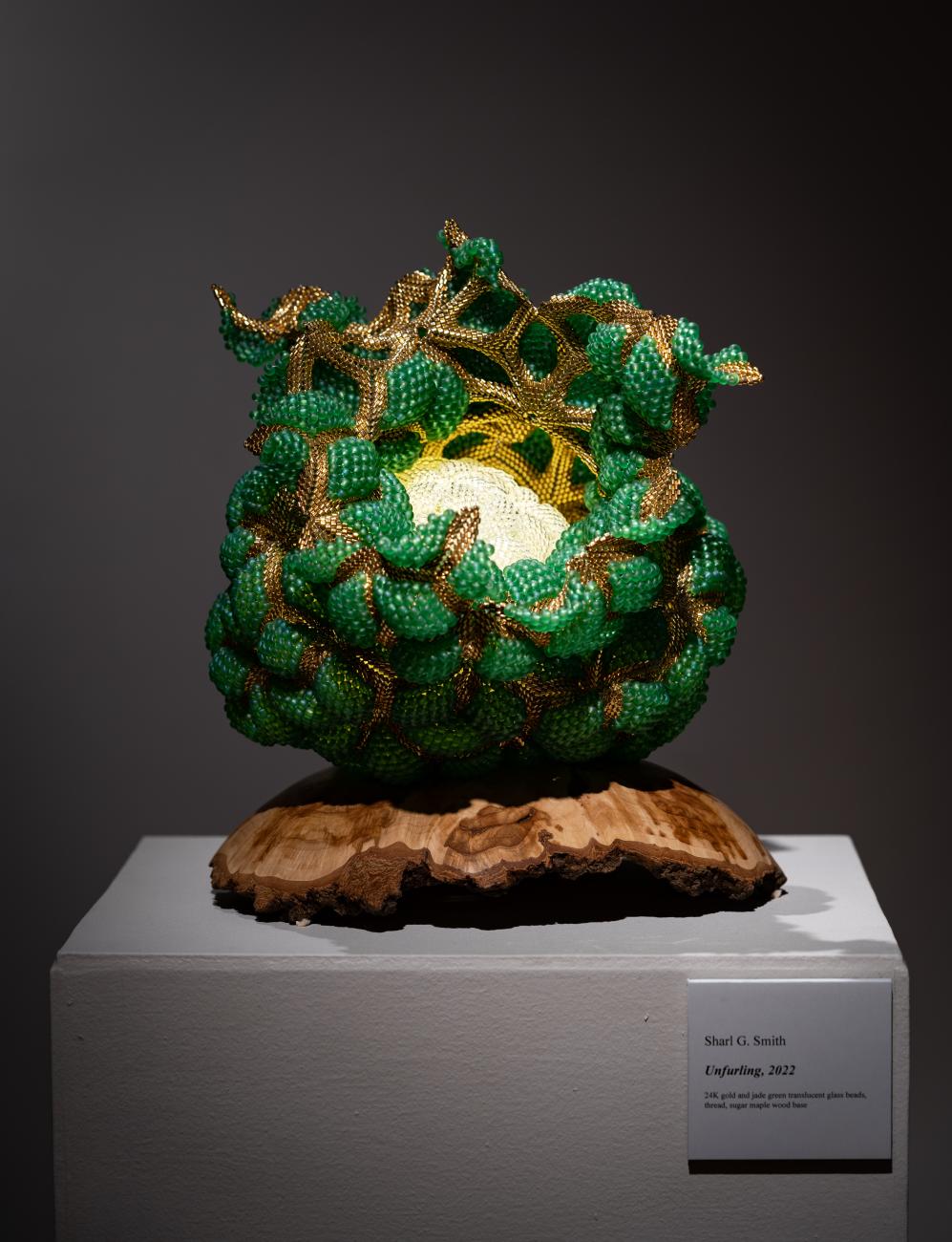 An image of Sharl G Smith's beaded sculpture Unfurling, which features a green outer shell that peels away in the centre to reveal a white beaded orb inside.
