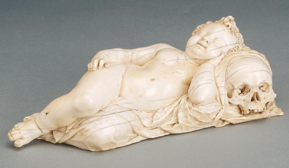 ivory sculpture of youth lying on their side on skull pillow