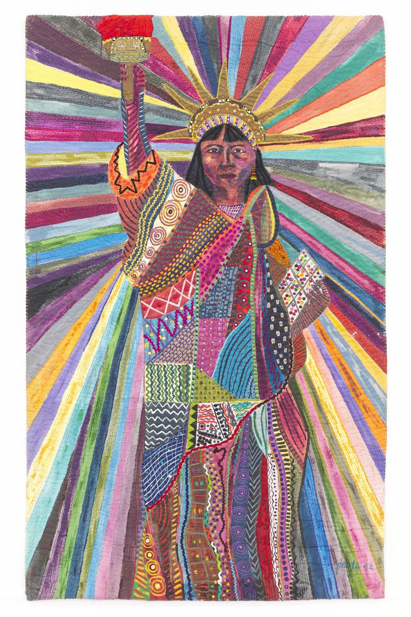 An image of Pacita Abad's trapunto L.A. Liberty. It reimagines the Lady of Liberty as a woman with brown skin, wearing a multi-coloured patchwork robe. Rays of colour shoot out from her crown
