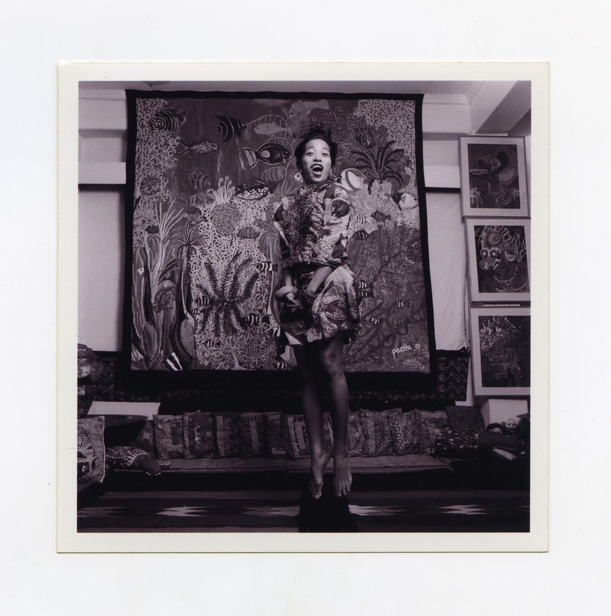 A black-and-white photograph of artist Pacita Abad with her work Puerto Galera I. She is jumping in front of her work