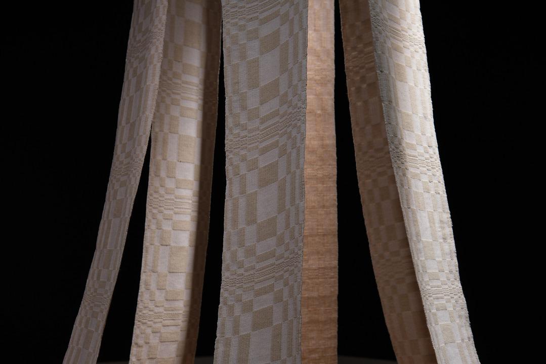 A detail shot of Carol Ann Apilado's work Channel. It features 7 beige and white weaved strips arranged in a circle