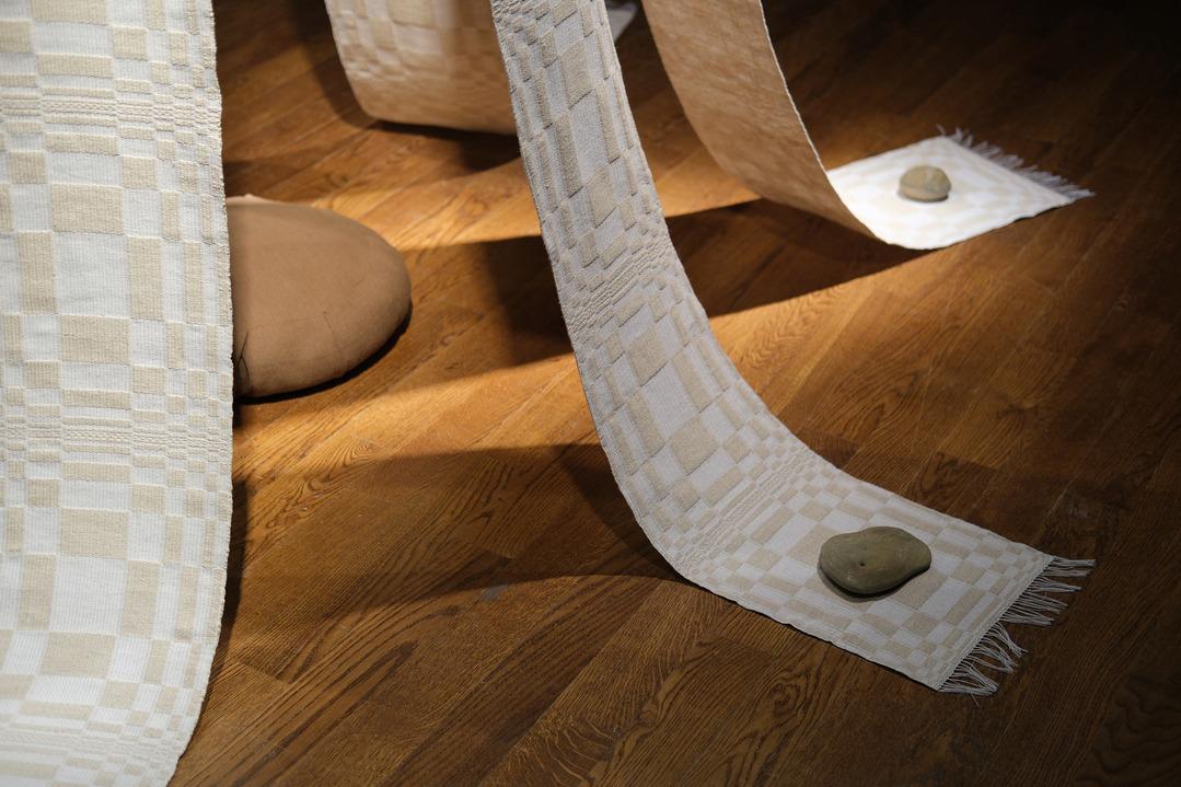 A detail shot of Carol Ann Apilado's work Channel (2023). It focuses on the bottom of the woven strips, which features rocks weighing down the ends