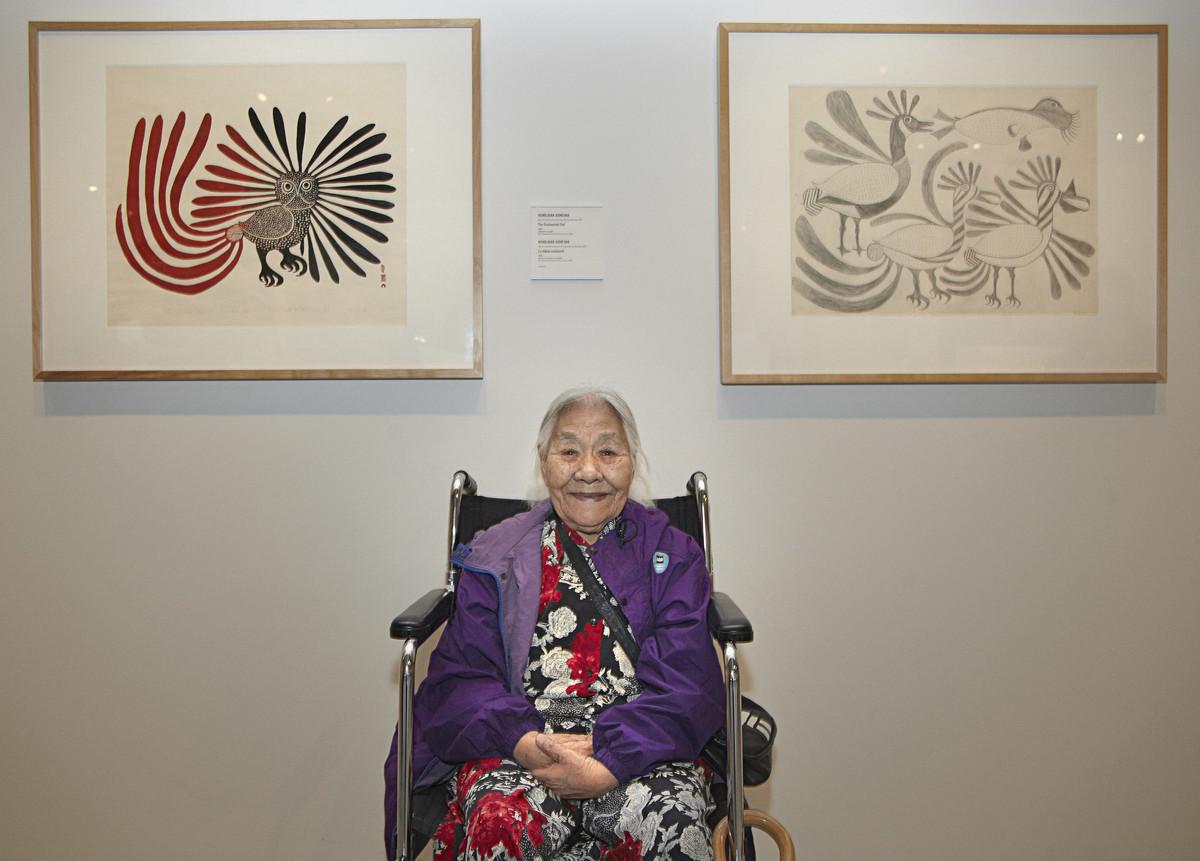 An image of Inuk artist Kenojuak Ashevak sitting in a wheelchair between two of her prints.
