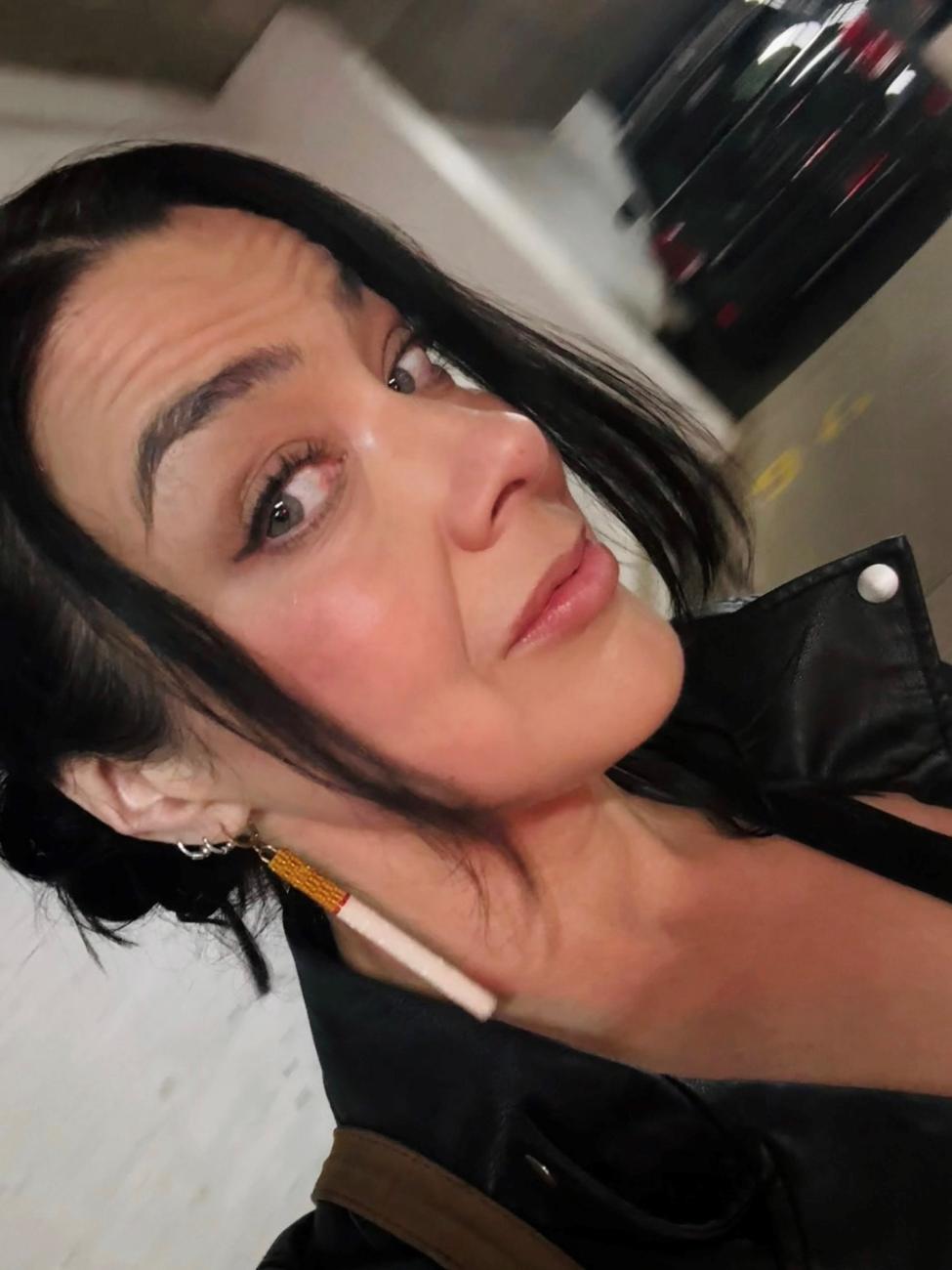 An image of artist Tarralik Duffy. A woman faces the viewer. She has long dark hair and earring that have pendants that look like cigarettes.