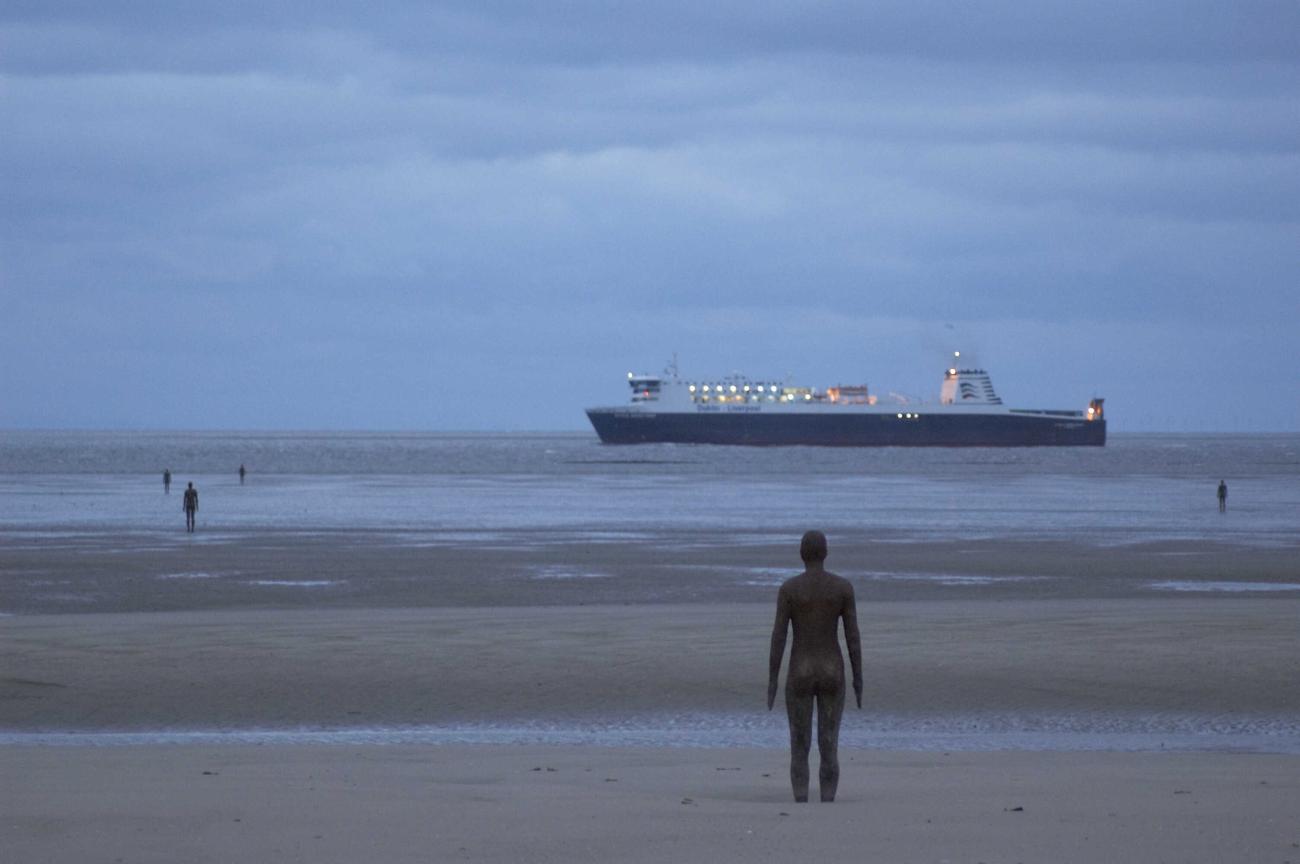 photo of Antony Gormley sculptures installed along shoreline looking out to sea