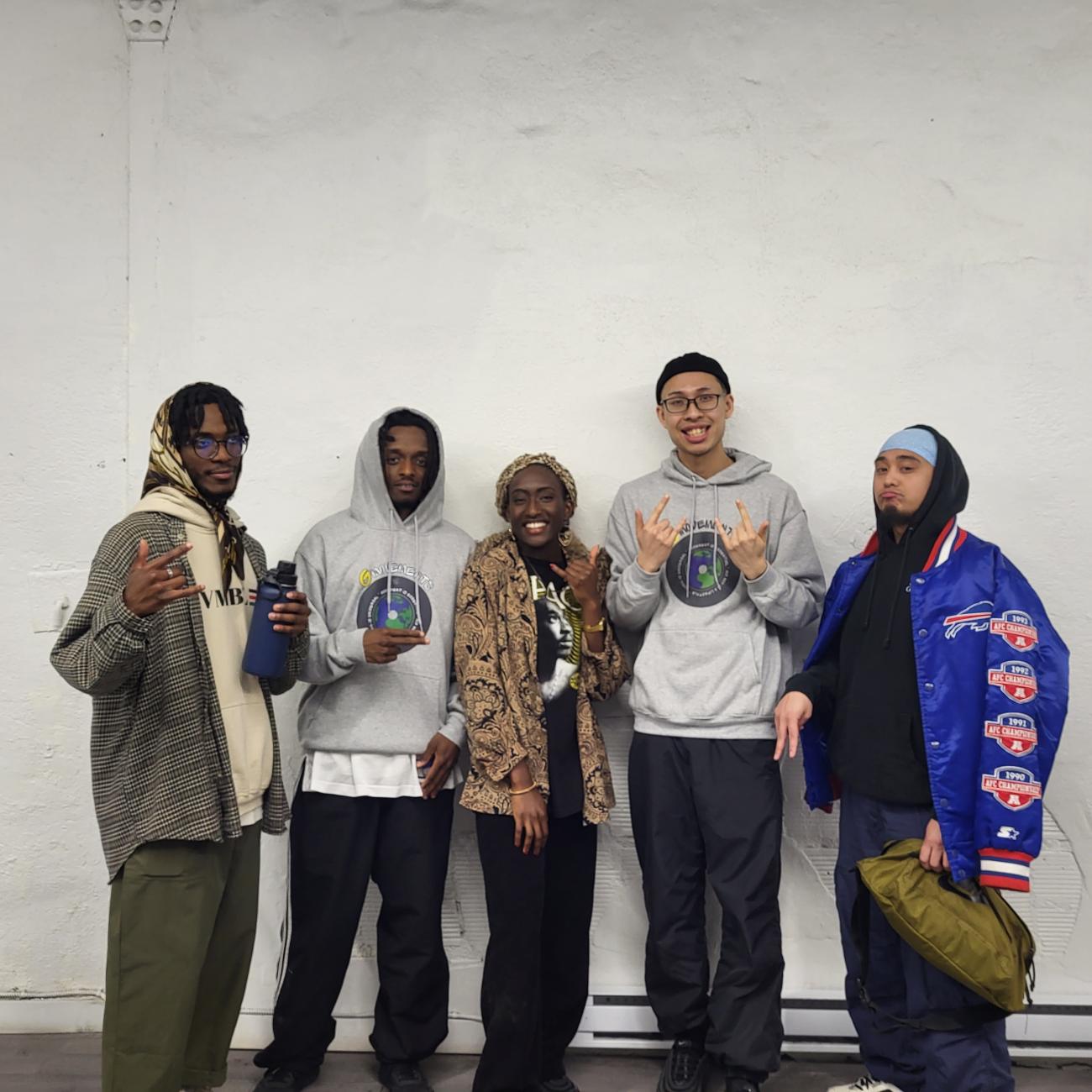 An photo of TBD crew members posing together against a white wall