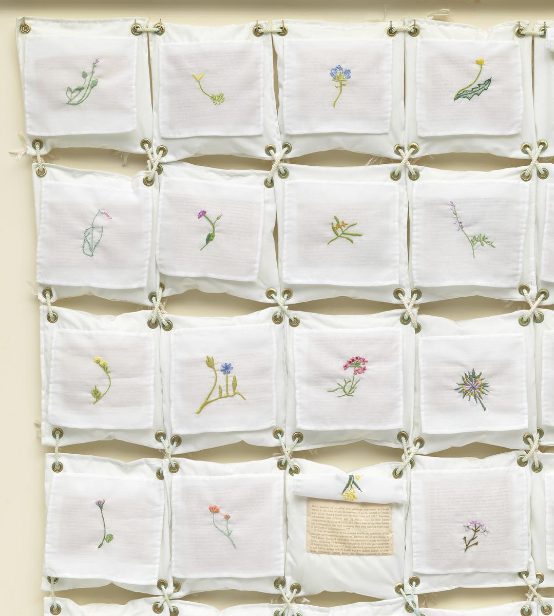 Small square pieces of fabric with small plants quilted on the centre. Each square is held together by rope.