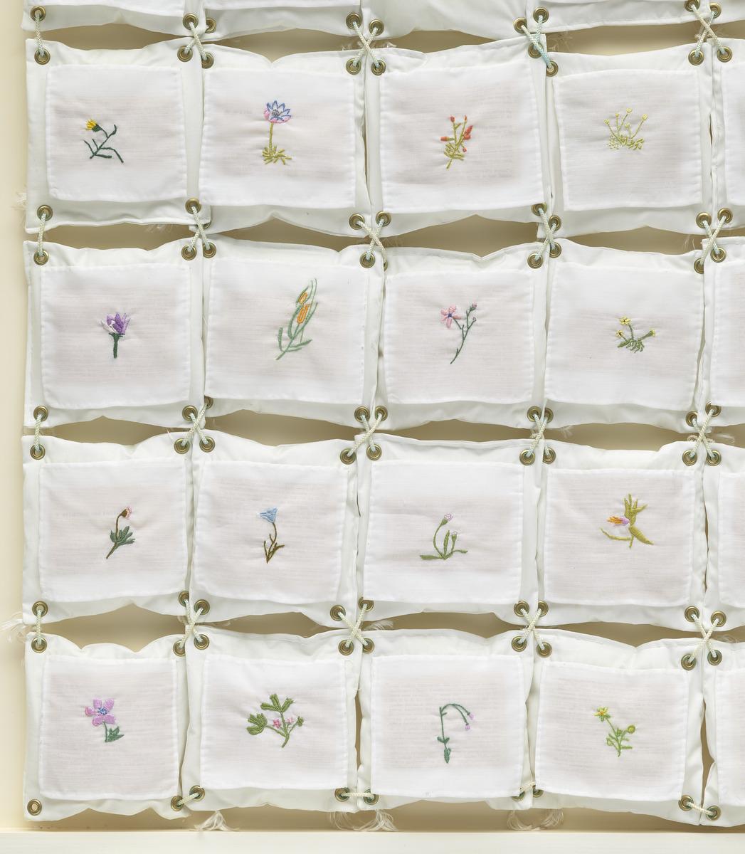 Small square pieces of fabric with small plants quilted on the centre. Each square is held together by rope.