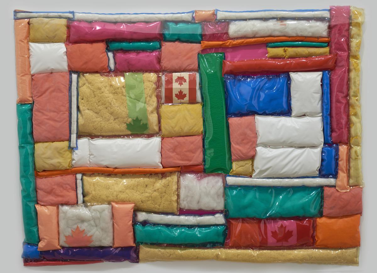 An image of Joyce Wieland's plastic work Confedspread. It features quilted rectangles covered in multicoloured plastics and contains Canadian Flags.