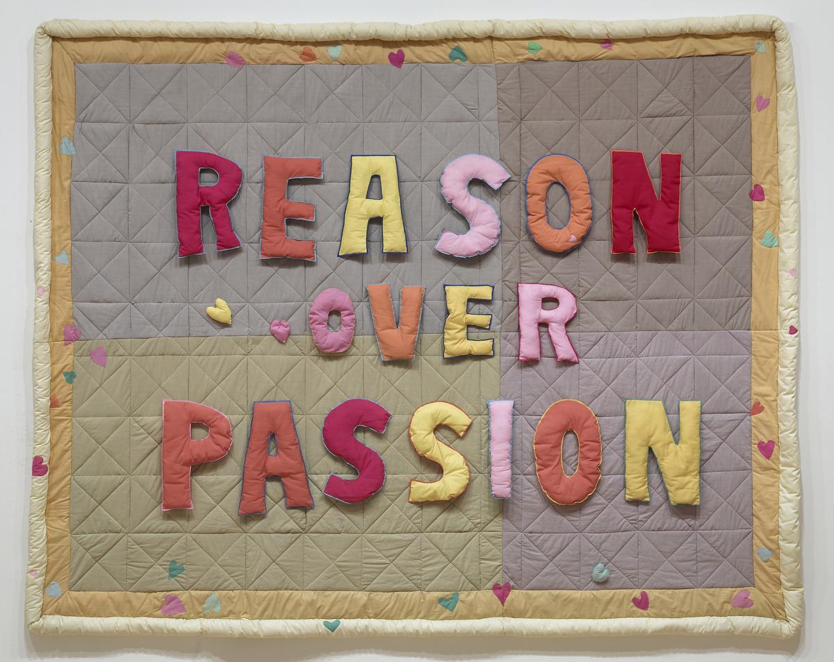 An image of Joyce Wieland's quilt Reason over Passion. It has the phrase "Reason Over Passion: in alternating red, yellow, pink, and orange block letters.