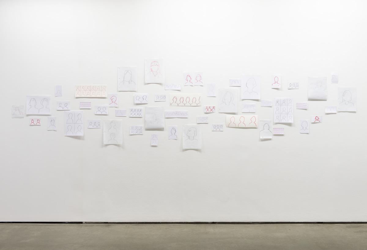 A photo of Faye HeavyShield's work I'll know you when I see you, which features silhouettes drawn on different sheets of white paper attached to a white wall