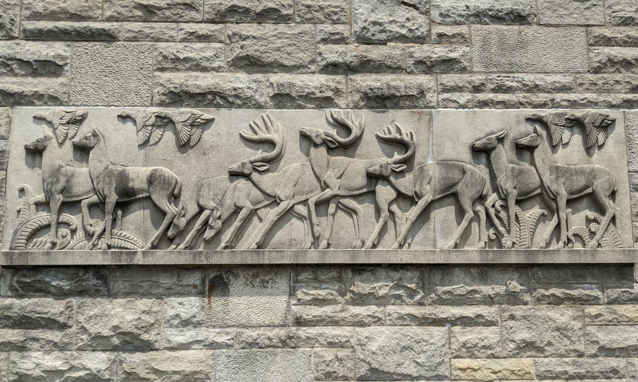 A stone wall featuring a relief sculpture of deer running across a field