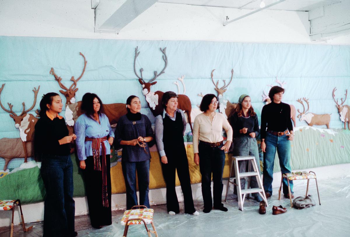 A photograph of Joyce Wieland, quilters, and assistants standing in front of the quilt Barren Ground Caribou