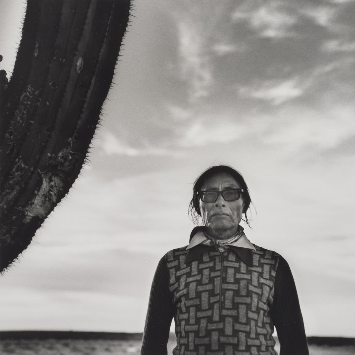 An image of Graciela Iturbide's photo Desierto de Sonora, México. It features a woman standing in a desert beside a cactus