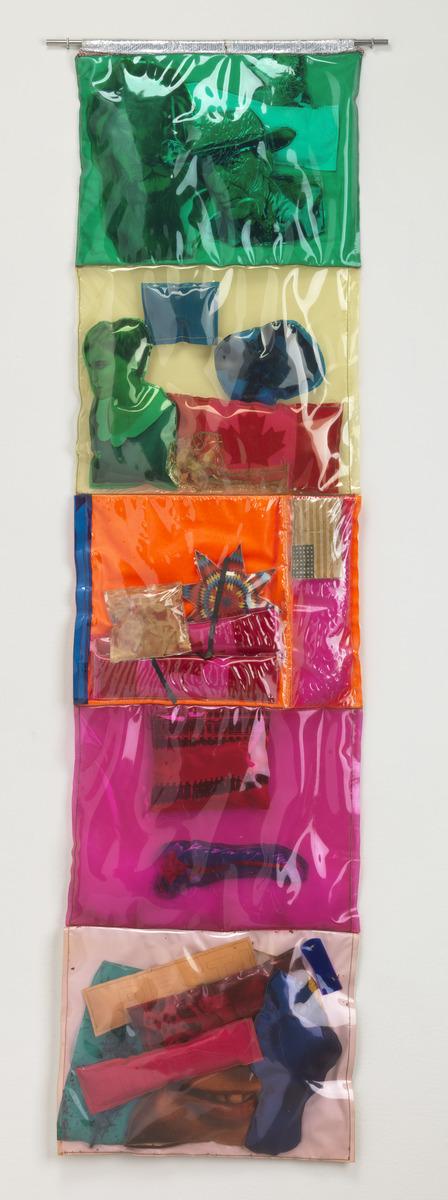 A photo of Joyce Wieland's plastic work, Stuffed Movie, which features 5 multi-colour squared filled with various items and attached as one long strip
